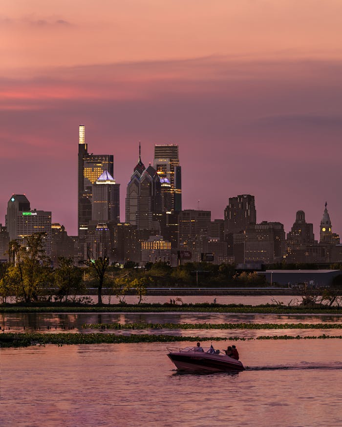 Dramatic skyline of Philadelphia at sunset with a motorboat on the water, capturing urban serenity.