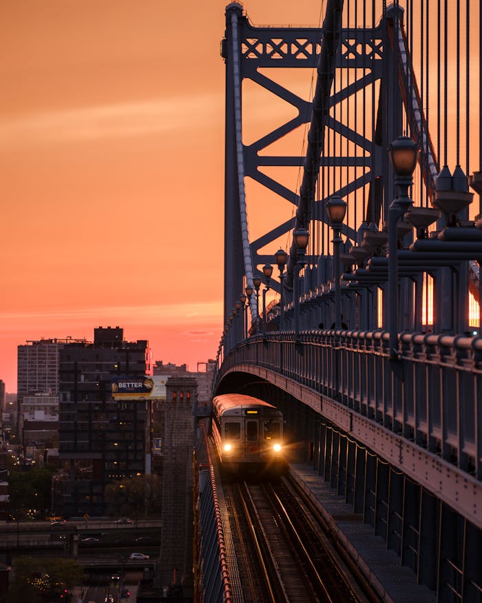 Train crossing the Benjamin Franklin Bridge at sunset in Philadelphia, showcasing cityscape views.